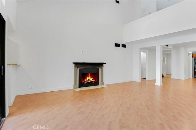 unfurnished living room with light hardwood / wood-style floors and a towering ceiling