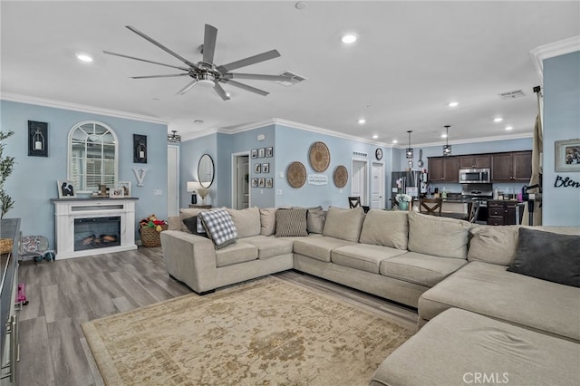 living room with light wood-type flooring, ceiling fan, and crown molding