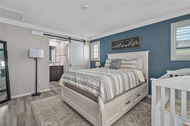 bedroom with light wood-type flooring, ensuite bathroom, a barn door, and ornamental molding