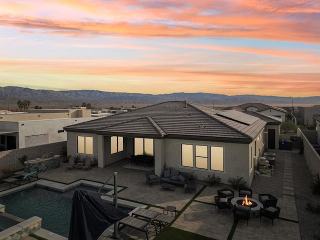 back house at dusk with a fenced in pool, a mountain view, a patio area, and a fire pit