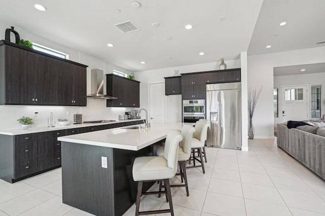 kitchen featuring appliances with stainless steel finishes, sink, a kitchen breakfast bar, a kitchen island with sink, and wall chimney exhaust hood