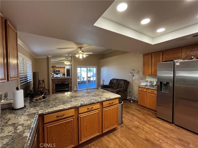 kitchen with kitchen peninsula, stainless steel refrigerator with ice dispenser, light hardwood / wood-style flooring, a raised ceiling, and light stone countertops