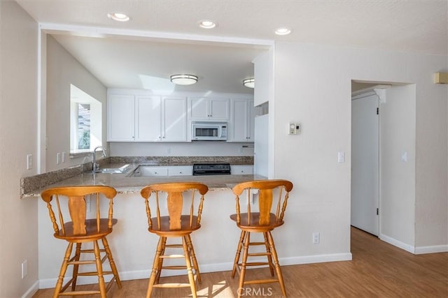 kitchen featuring a breakfast bar, sink, kitchen peninsula, white cabinets, and stove