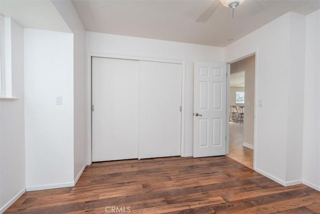 unfurnished bedroom with dark wood-type flooring, a closet, and ceiling fan