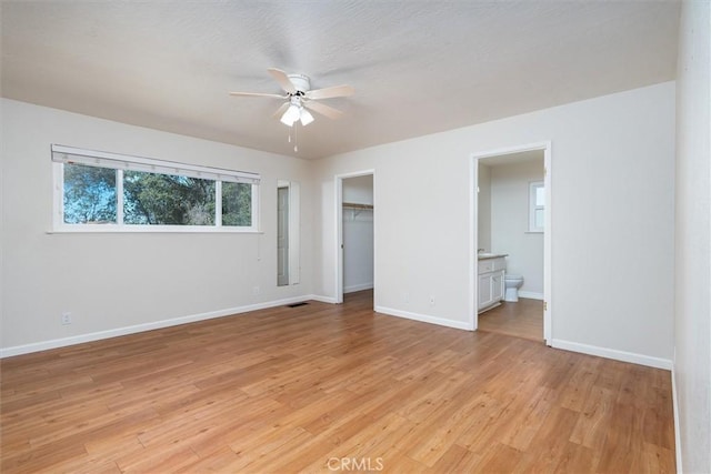 unfurnished bedroom featuring ensuite bath, ceiling fan, light hardwood / wood-style floors, a spacious closet, and a closet