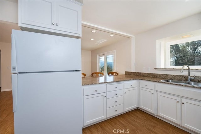 kitchen with sink, white cabinetry, dark stone countertops, white refrigerator, and light hardwood / wood-style floors