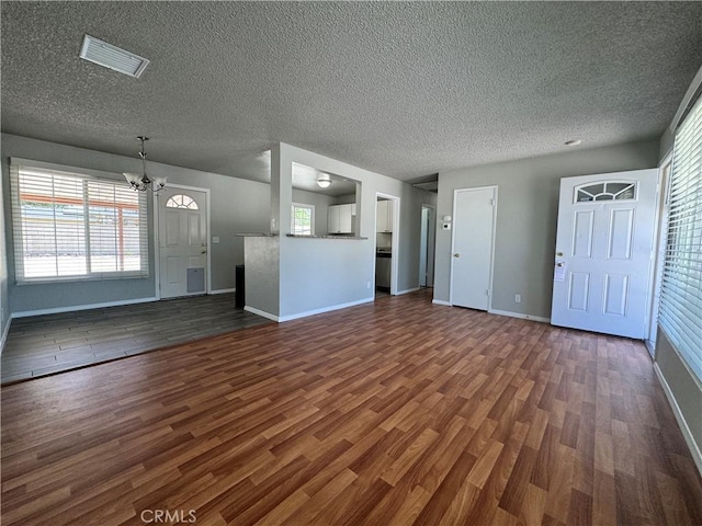 unfurnished living room featuring an inviting chandelier, a textured ceiling, and dark hardwood / wood-style floors