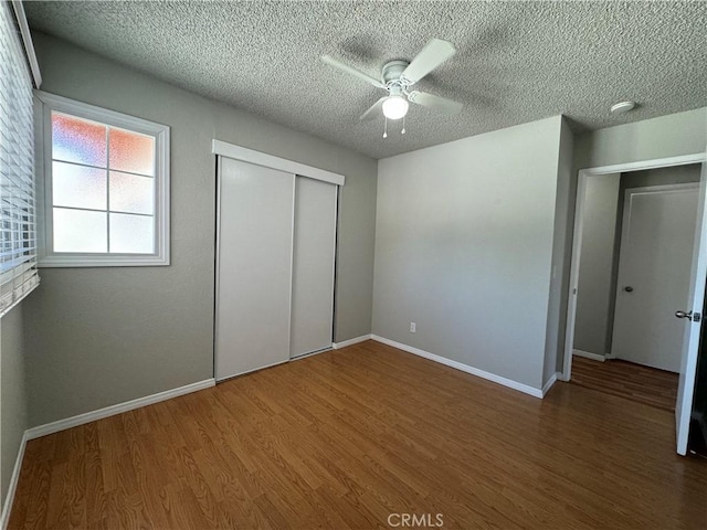 unfurnished bedroom featuring ceiling fan, a textured ceiling, dark hardwood / wood-style floors, and a closet