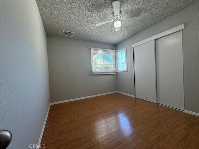 unfurnished bedroom with wood-type flooring, a textured ceiling, a closet, and ceiling fan