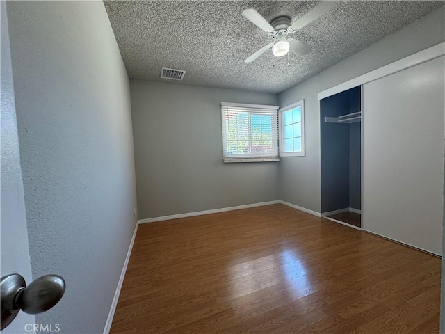 unfurnished bedroom with hardwood / wood-style floors, a textured ceiling, a closet, and ceiling fan