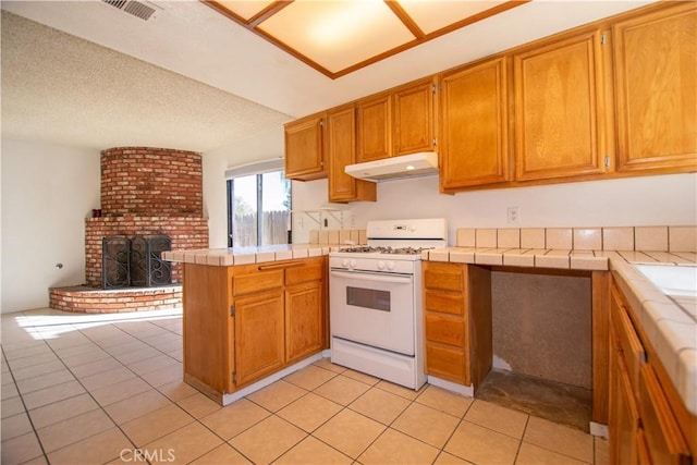 kitchen featuring gas range gas stove, tile counters, open floor plan, a peninsula, and under cabinet range hood