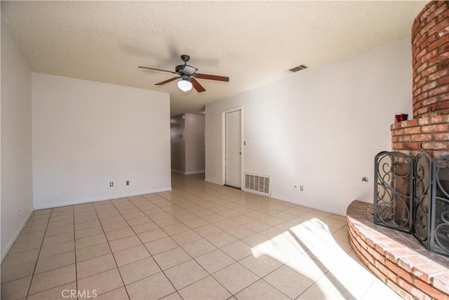 unfurnished living room featuring light tile patterned floors, ceiling fan, a brick fireplace, and visible vents