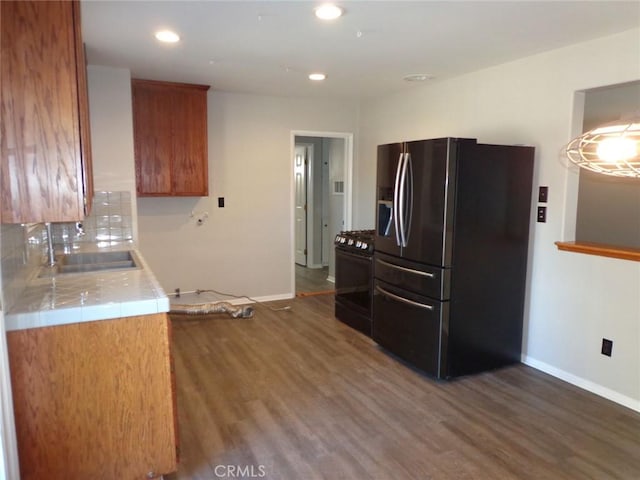 kitchen with dark wood-type flooring, stainless steel gas stove, sink, tile countertops, and fridge with ice dispenser