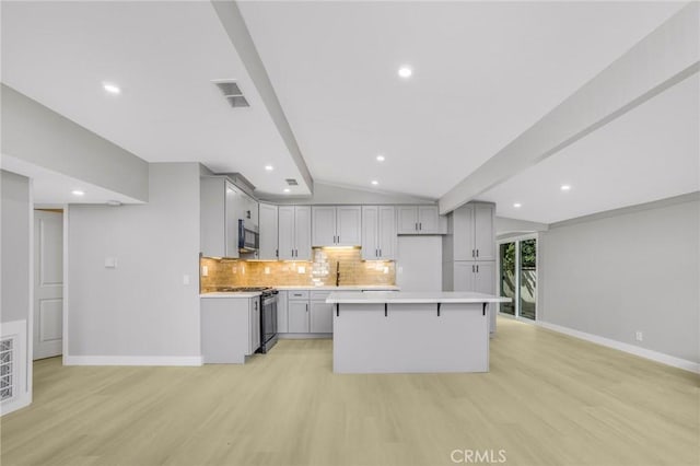 kitchen featuring gas range, light wood-type flooring, gray cabinetry, a center island, and vaulted ceiling with beams