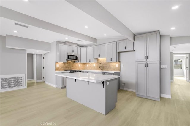 kitchen featuring a kitchen island, a kitchen bar, light hardwood / wood-style floors, and gray cabinets