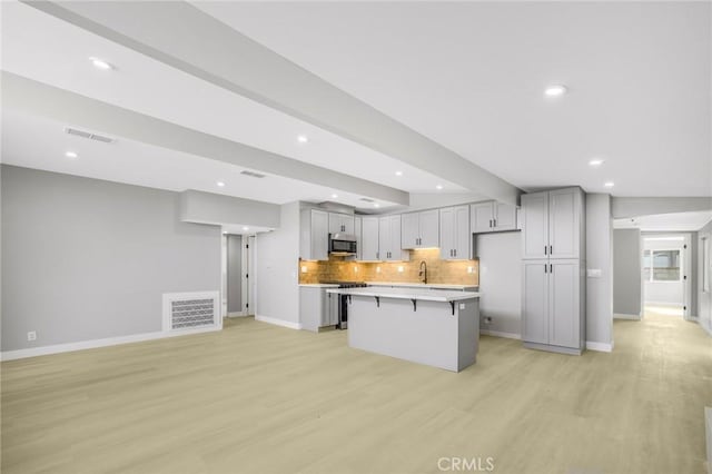 kitchen with a kitchen island, light hardwood / wood-style flooring, gray cabinetry, and a breakfast bar