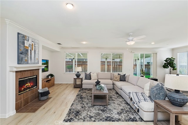 living room featuring ceiling fan, light hardwood / wood-style flooring, crown molding, and a tiled fireplace