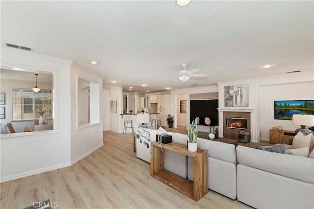 living room featuring ceiling fan, light hardwood / wood-style flooring, crown molding, and a tiled fireplace