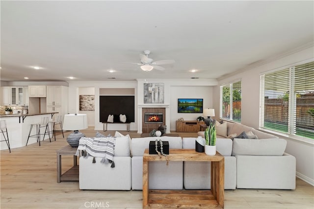 living room with ceiling fan, a tile fireplace, crown molding, and light wood-type flooring