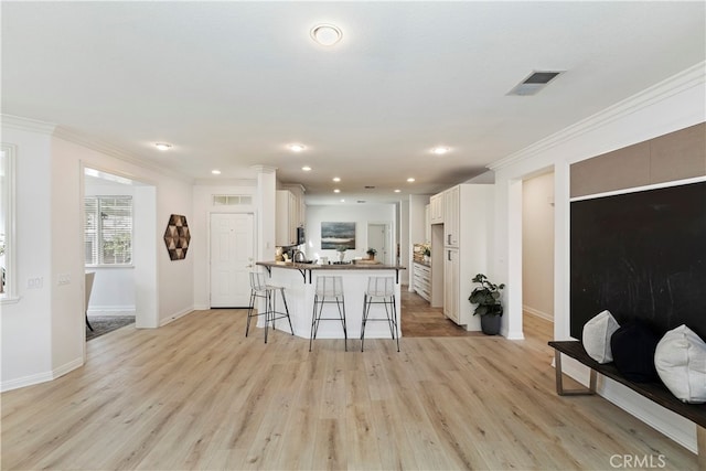 kitchen with a kitchen breakfast bar, kitchen peninsula, light hardwood / wood-style flooring, white cabinets, and ornamental molding