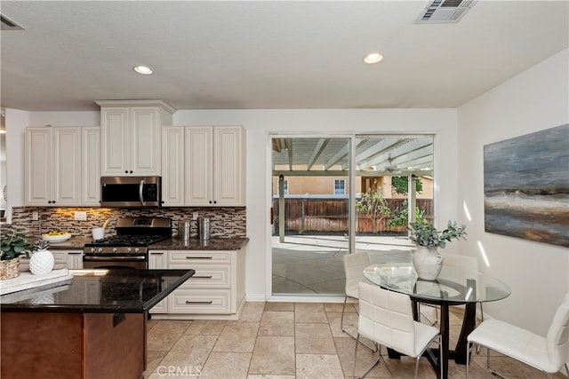 kitchen with backsplash, white cabinets, stainless steel appliances, and dark stone counters