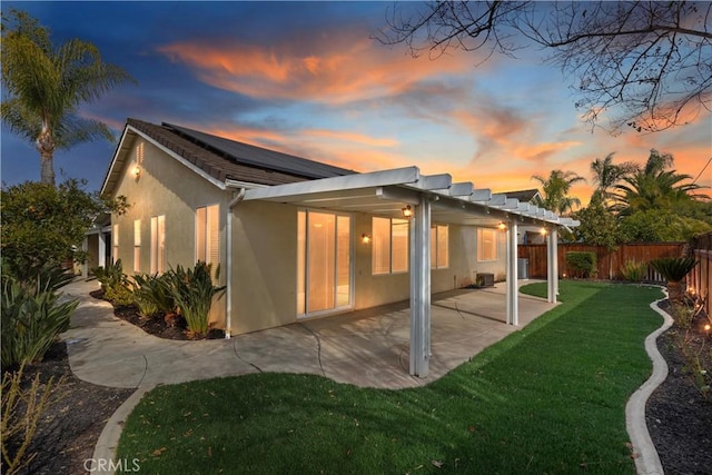 back house at dusk with a patio area, a lawn, and a pergola