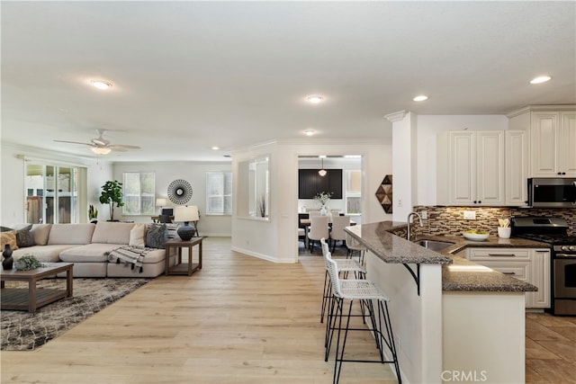 kitchen featuring kitchen peninsula, appliances with stainless steel finishes, sink, white cabinetry, and a breakfast bar