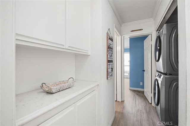 clothes washing area with light hardwood / wood-style floors, cabinets, ornamental molding, and stacked washer and dryer