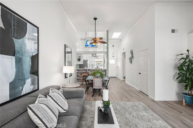 living room featuring a high ceiling, a skylight, ornamental molding, light wood-type flooring, and ceiling fan