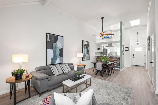 living room featuring hardwood / wood-style floors, a skylight, ceiling fan, high vaulted ceiling, and beam ceiling