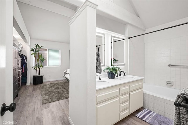 bathroom with hardwood / wood-style flooring, vanity, tiled shower / bath, and vaulted ceiling