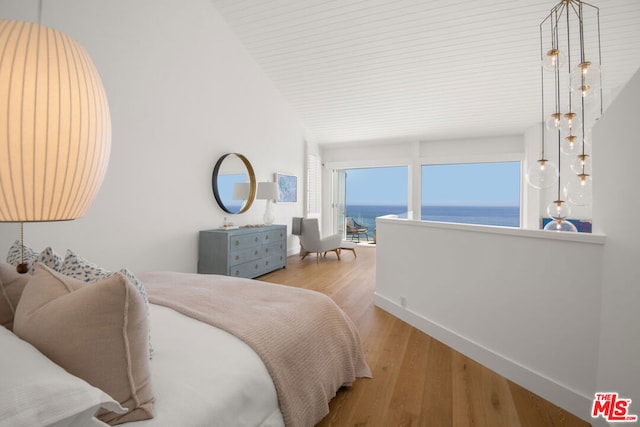 bedroom with light hardwood / wood-style floors, a water view, and vaulted ceiling