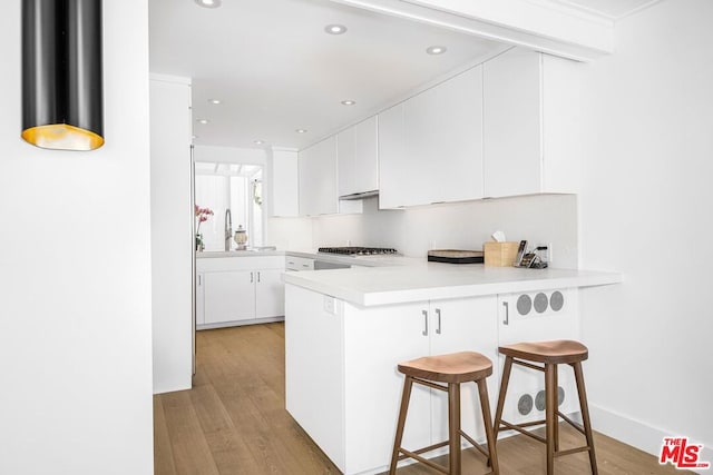 kitchen with light hardwood / wood-style floors, white cabinetry, sink, kitchen peninsula, and a breakfast bar