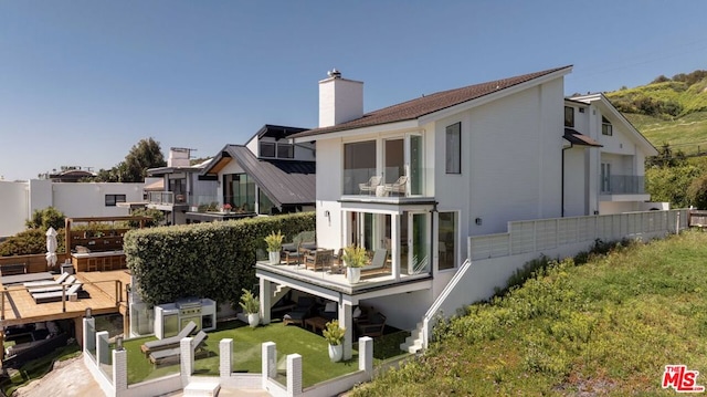 rear view of house with a balcony, a lawn, and a patio