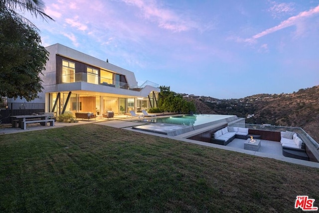 exterior space featuring a balcony, a patio area, a yard, and an outdoor living space with a fire pit