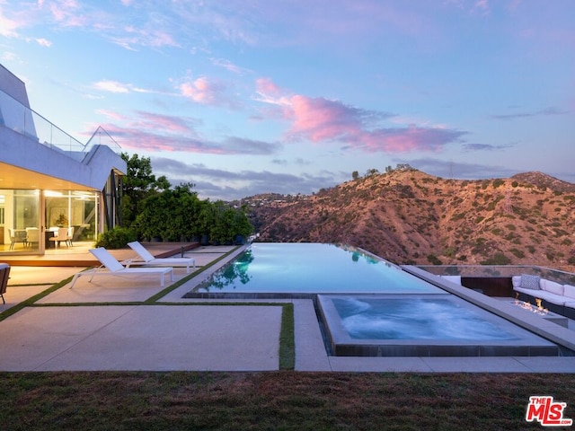 pool at dusk featuring a mountain view and a patio