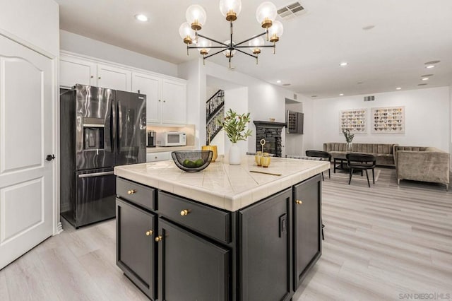 kitchen with white cabinetry, stainless steel fridge with ice dispenser, tile countertops, a kitchen island, and light hardwood / wood-style floors