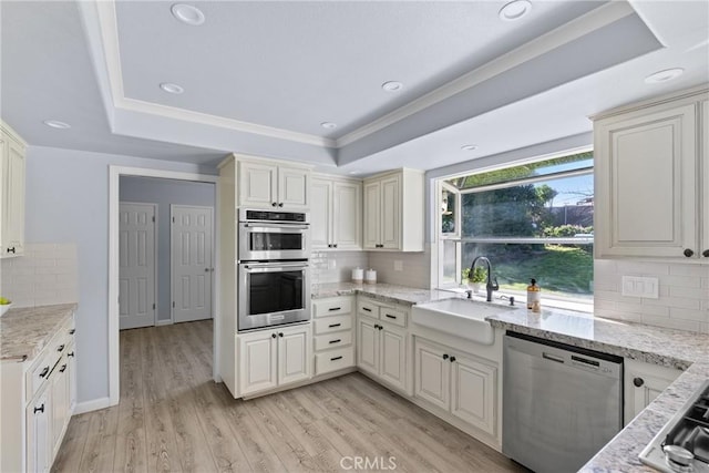 kitchen with backsplash, light hardwood / wood-style flooring, a raised ceiling, and stainless steel appliances