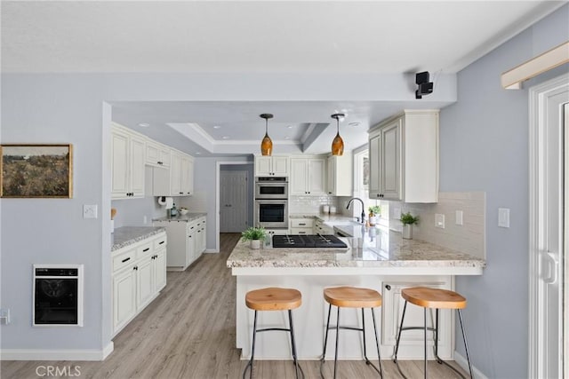 kitchen featuring kitchen peninsula, hanging light fixtures, a raised ceiling, sink, and decorative backsplash