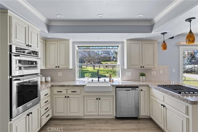 kitchen with crown molding, pendant lighting, sink, cream cabinetry, and stainless steel appliances