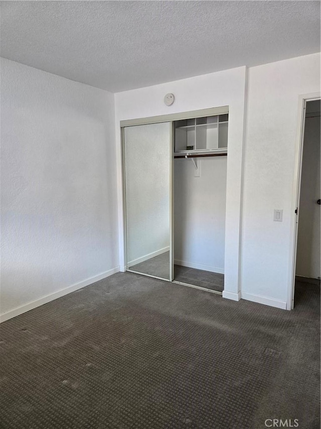 unfurnished bedroom featuring a textured ceiling, dark carpet, and a closet