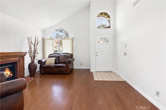 entrance foyer featuring a brick fireplace, hardwood / wood-style floors, and high vaulted ceiling