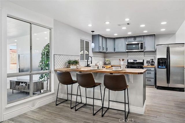 kitchen featuring a kitchen bar, butcher block counters, gray cabinets, kitchen peninsula, and stainless steel appliances