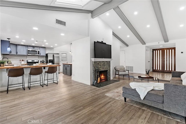 living room with high vaulted ceiling, a fireplace, beamed ceiling, sink, and light hardwood / wood-style floors