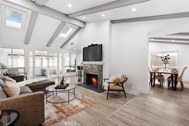 living room featuring beamed ceiling, high vaulted ceiling, a skylight, and light hardwood / wood-style floors