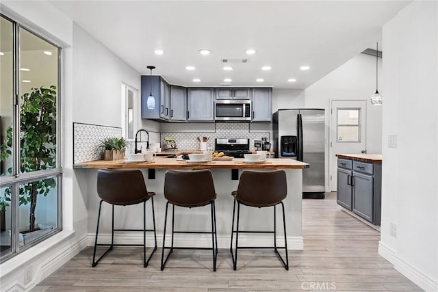 kitchen featuring stainless steel appliances, hanging light fixtures, wood counters, and a kitchen bar