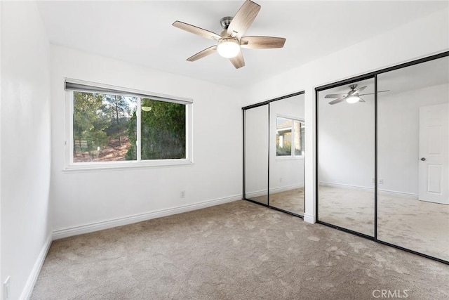 unfurnished bedroom with multiple closets, multiple windows, ceiling fan, and light carpet