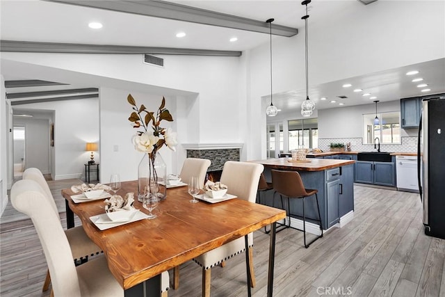 dining room featuring sink, lofted ceiling with beams, and light hardwood / wood-style flooring