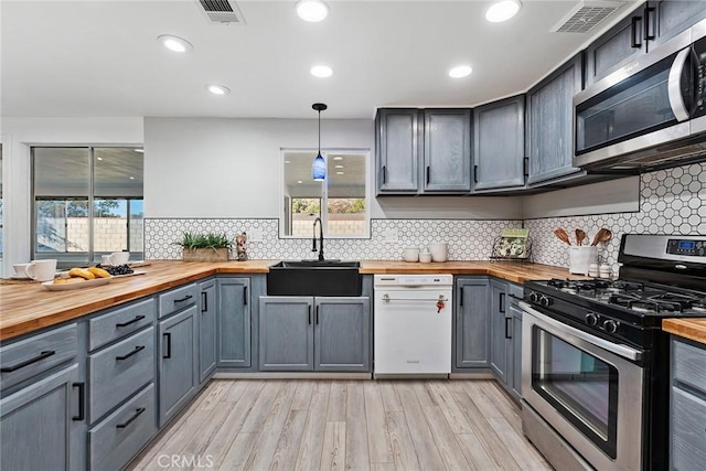 kitchen featuring butcher block counters, sink, gray cabinetry, decorative light fixtures, and appliances with stainless steel finishes