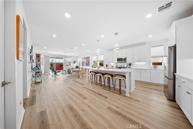 kitchen with appliances with stainless steel finishes, a center island with sink, light hardwood / wood-style floors, white cabinets, and a kitchen bar